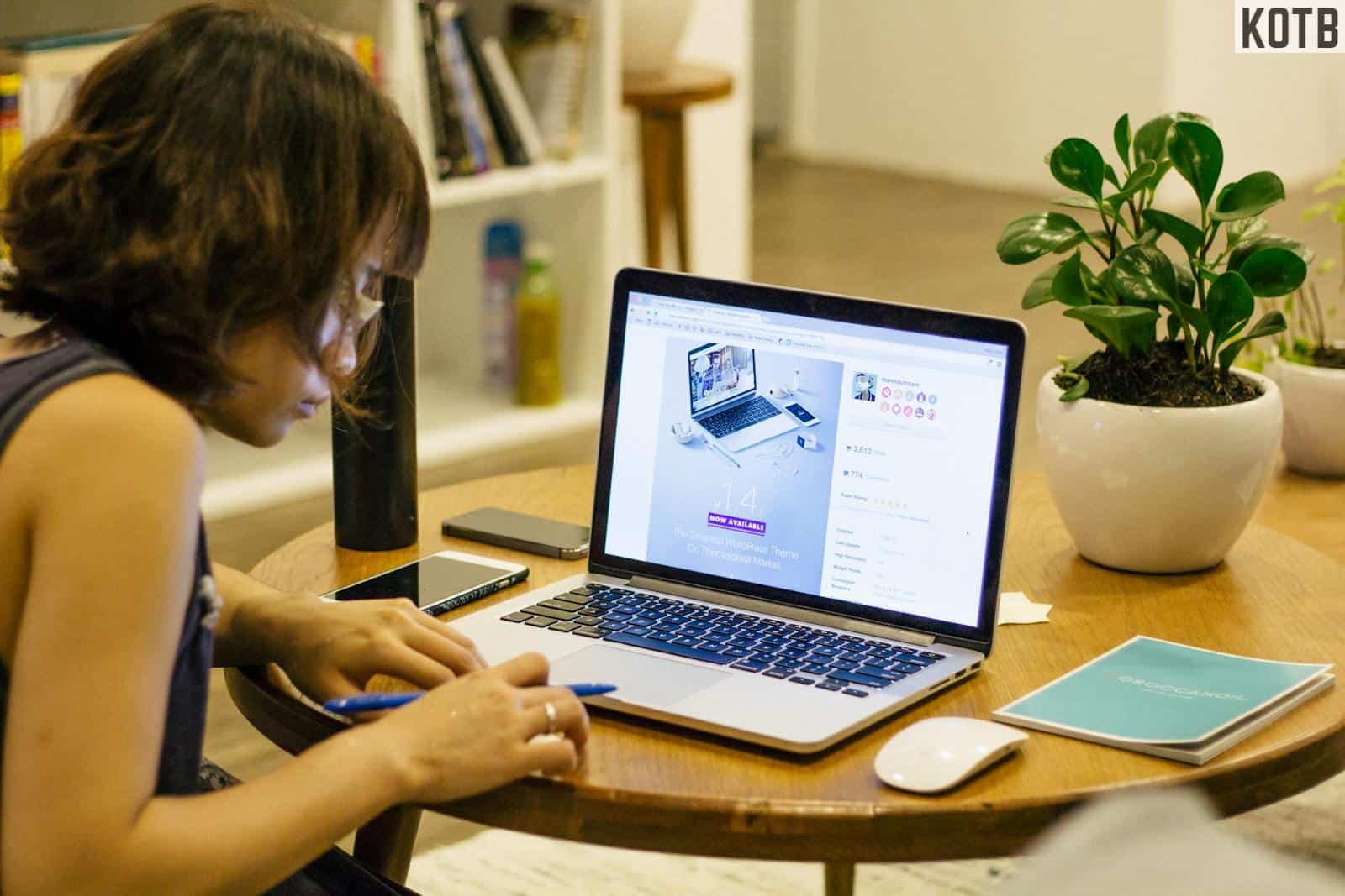 Woman in Black Tank Shirt Facing a Black Laptop Computer on Brown Wooden Round Table
