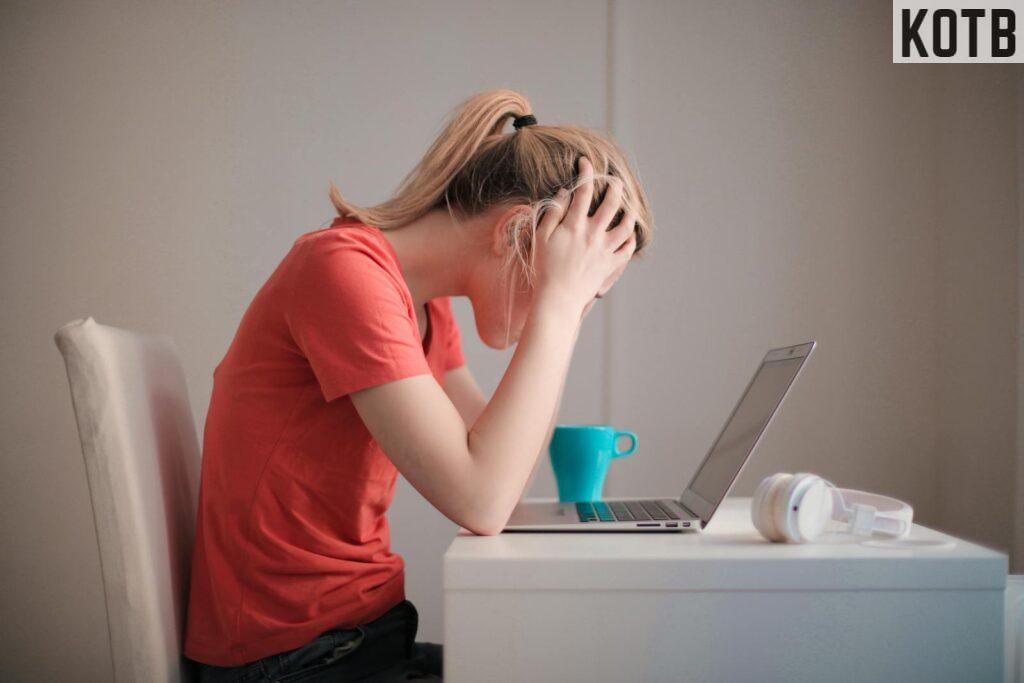 Young woman feeling stressed while studying at home with a laptop and coffee cup.