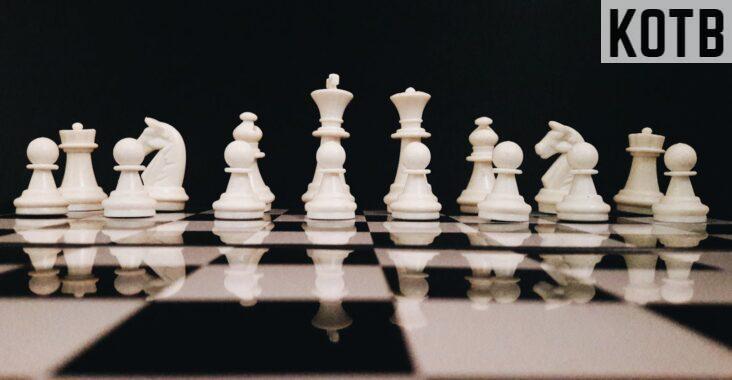 White chess pieces strategically placed on a board reflecting against a black background.