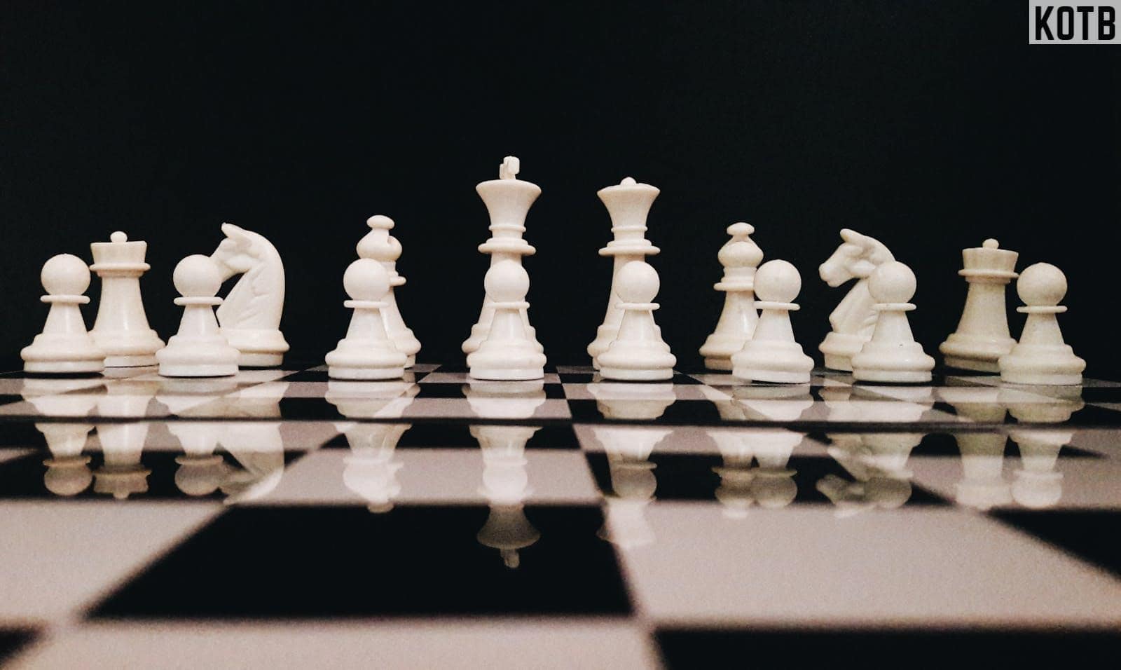 White chess pieces strategically placed on a board reflecting against a black background.